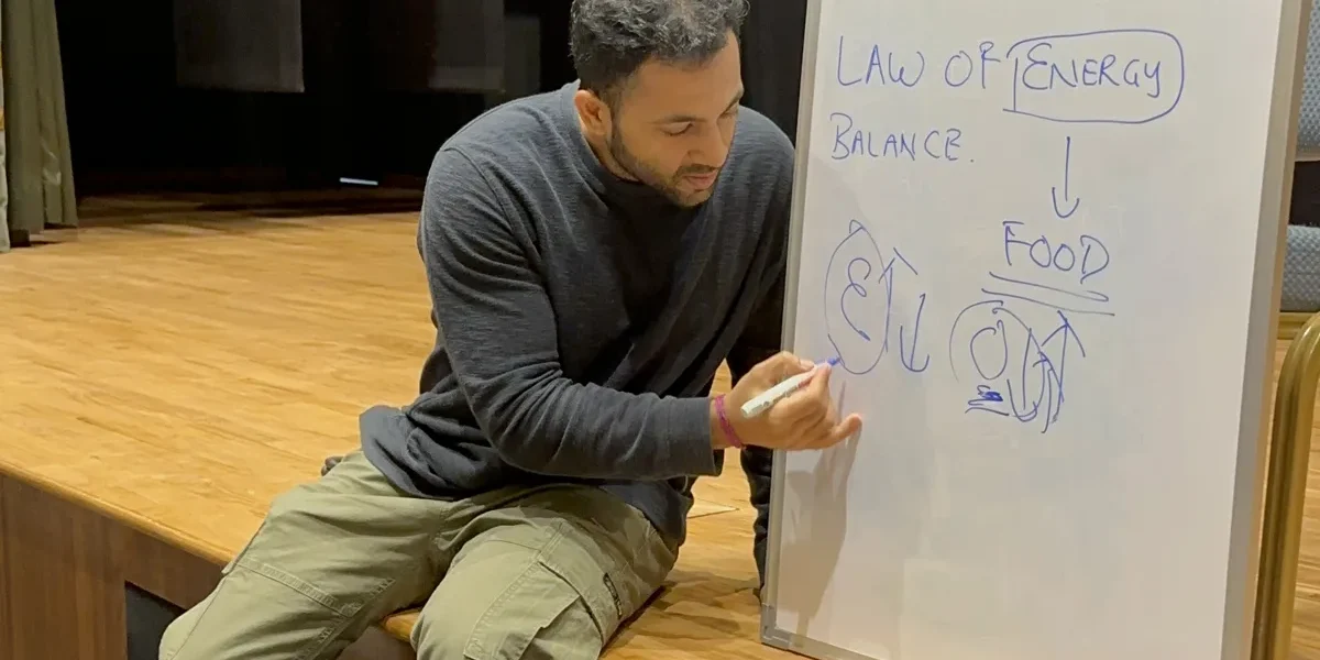 Coach Pankaj Narsian writing the law of energy balance on a whiteboard at a nutrition seminar